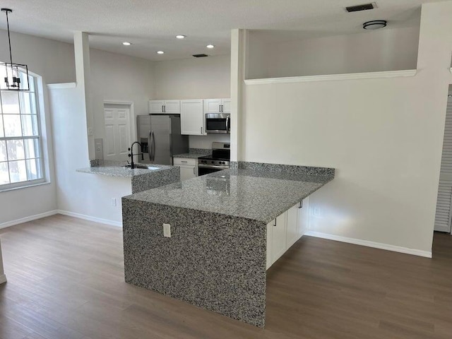 kitchen featuring appliances with stainless steel finishes, hanging light fixtures, kitchen peninsula, white cabinets, and stone countertops