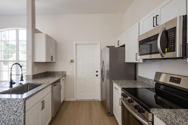 kitchen with appliances with stainless steel finishes, light hardwood / wood-style floors, light stone counters, sink, and white cabinetry