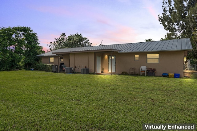 back house at dusk with a yard and central air condition unit