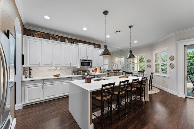 kitchen featuring stainless steel appliances, a center island with sink, white cabinetry, and pendant lighting