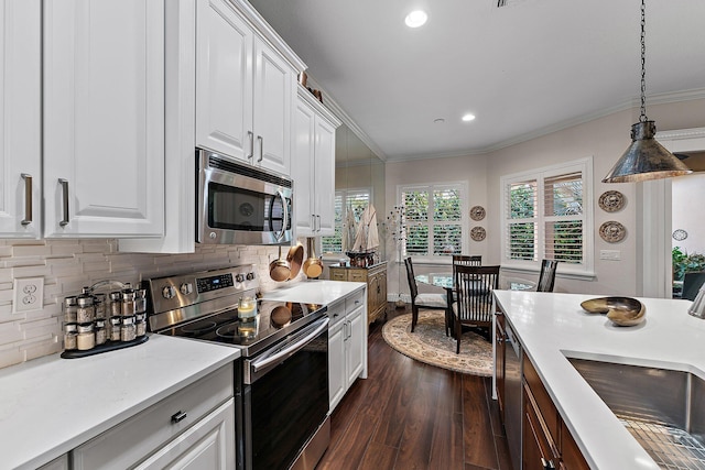 kitchen with white cabinetry, stainless steel appliances, tasteful backsplash, ornamental molding, and decorative light fixtures