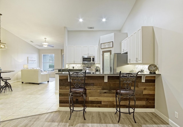 kitchen with white cabinetry, kitchen peninsula, stainless steel appliances, tasteful backsplash, and a breakfast bar