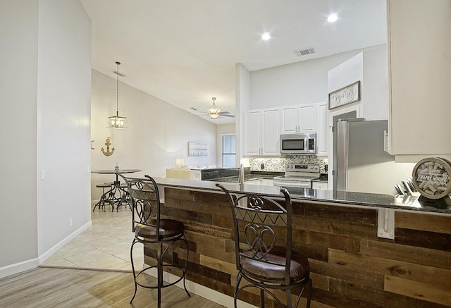 kitchen featuring lofted ceiling, kitchen peninsula, white cabinetry, appliances with stainless steel finishes, and a breakfast bar area