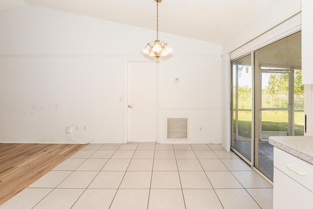 unfurnished dining area featuring light tile patterned flooring, vaulted ceiling, and a chandelier