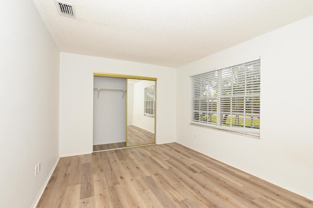 unfurnished bedroom with a textured ceiling, a closet, and light hardwood / wood-style floors