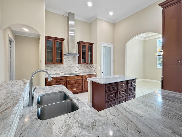 kitchen with sink, backsplash, light stone countertops, a kitchen island, and wall chimney exhaust hood