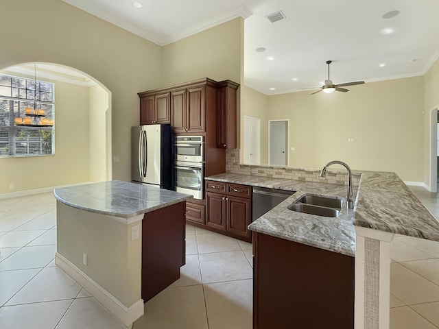 kitchen featuring sink, light tile patterned floors, appliances with stainless steel finishes, a kitchen island with sink, and ornamental molding