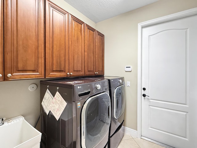 laundry room with sink, light tile patterned floors, washing machine and dryer, cabinets, and a textured ceiling