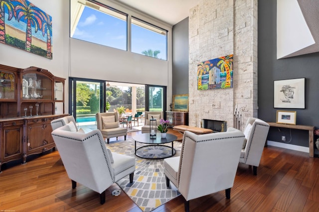 living room featuring a towering ceiling, hardwood / wood-style floors, and a stone fireplace