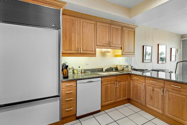 kitchen featuring built in fridge, sink, dishwasher, and dark stone counters