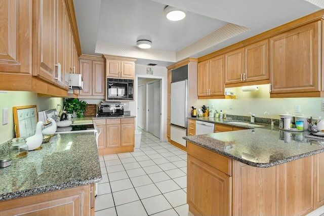 kitchen with kitchen peninsula, sink, built in appliances, light tile patterned floors, and dark stone counters