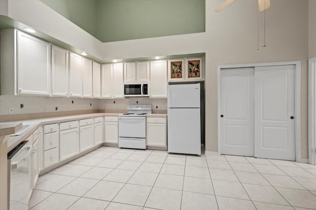 kitchen with white appliances, light tile patterned flooring, a high ceiling, and white cabinetry