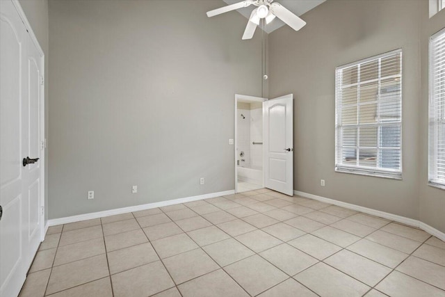 empty room featuring ceiling fan, a high ceiling, and light tile patterned floors