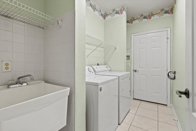 laundry room with tile walls, washing machine and clothes dryer, light tile patterned floors, and sink