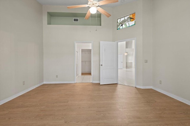 unfurnished bedroom with a high ceiling, a closet, light hardwood / wood-style floors, a walk in closet, and ceiling fan