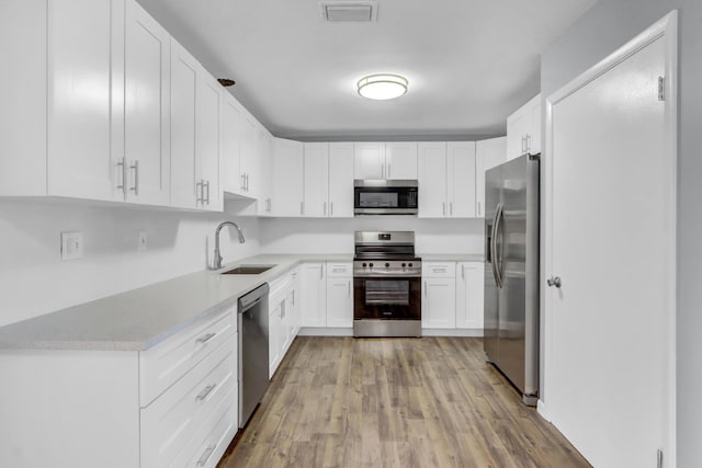 kitchen with light wood-type flooring, appliances with stainless steel finishes, white cabinetry, and sink