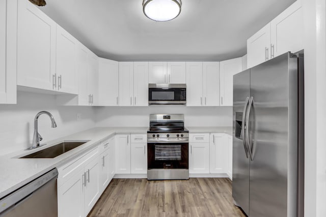 kitchen with stainless steel appliances, sink, white cabinetry, light stone counters, and light hardwood / wood-style floors