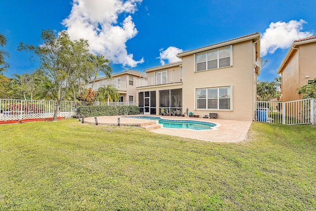 rear view of property featuring a lawn, a patio, a balcony, and a fenced in pool