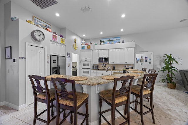 kitchen with a kitchen bar, white cabinetry, stainless steel appliances, a large island, and light tile patterned floors