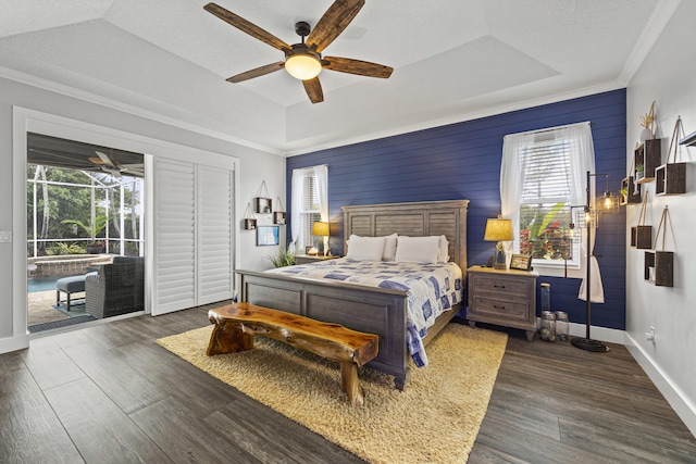 bedroom featuring ceiling fan, wood walls, a tray ceiling, and dark wood-type flooring