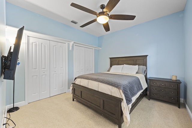 bedroom featuring light carpet, ceiling fan, and two closets