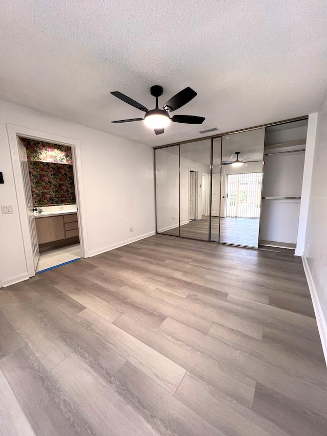 unfurnished bedroom with ceiling fan, hardwood / wood-style flooring, a textured ceiling, and ensuite bathroom