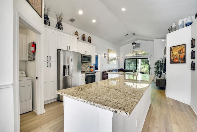 kitchen featuring lofted ceiling, a kitchen island, appliances with stainless steel finishes, washer / clothes dryer, and white cabinetry