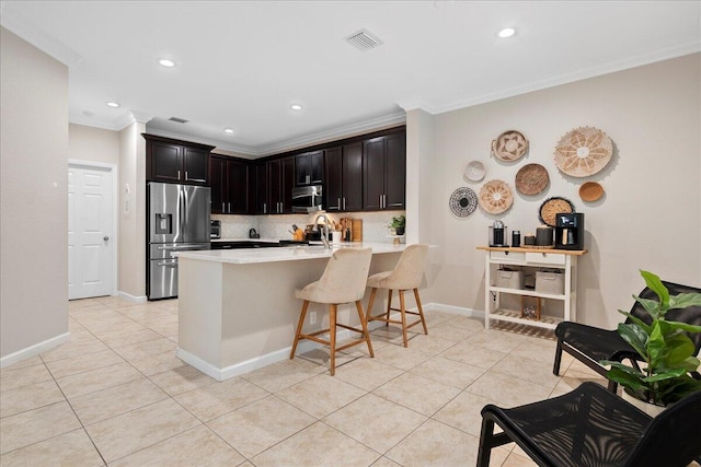 kitchen with light tile patterned floors, appliances with stainless steel finishes, backsplash, a kitchen breakfast bar, and ornamental molding