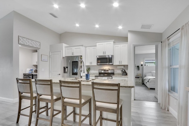 kitchen featuring white cabinets, a kitchen breakfast bar, light stone countertops, a center island with sink, and appliances with stainless steel finishes