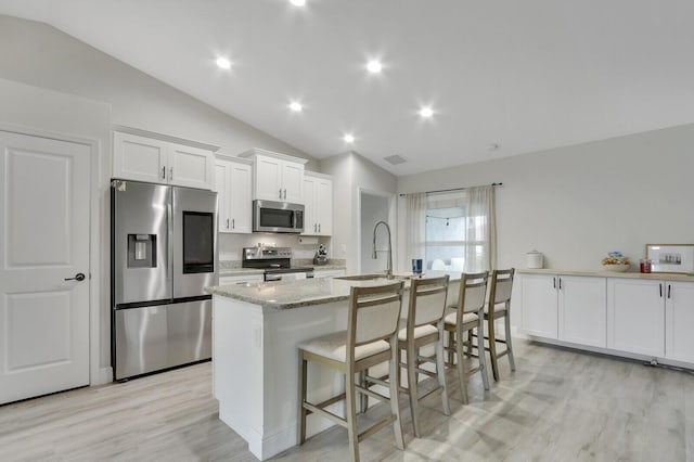 kitchen featuring a kitchen island with sink, vaulted ceiling, appliances with stainless steel finishes, a breakfast bar, and white cabinets