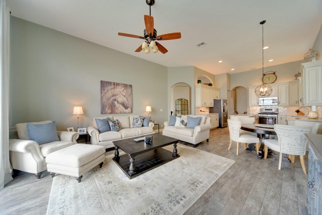 living room with ceiling fan with notable chandelier and light hardwood / wood-style floors