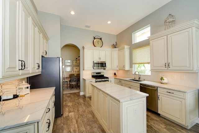 kitchen with sink, light stone counters, a center island, stainless steel appliances, and hardwood / wood-style floors