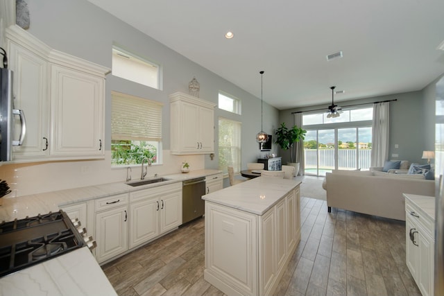 kitchen with sink, appliances with stainless steel finishes, light stone counters, a kitchen island, and decorative light fixtures