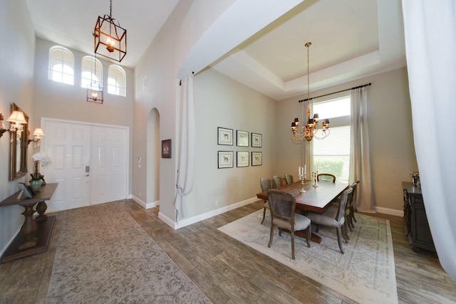 dining room with an inviting chandelier, a towering ceiling, a tray ceiling, and hardwood / wood-style floors