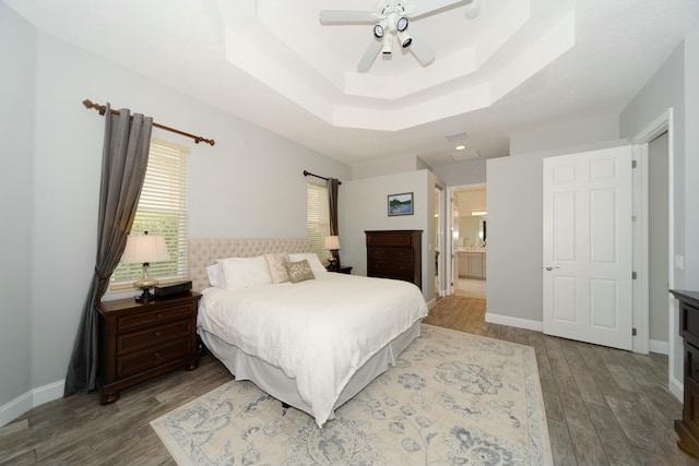 bedroom with hardwood / wood-style flooring, connected bathroom, ceiling fan, and a tray ceiling