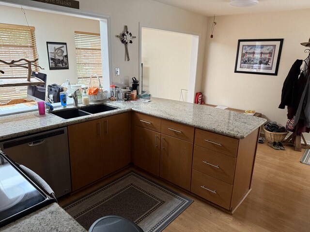 kitchen with sink, stainless steel dishwasher, light stone counters, kitchen peninsula, and light hardwood / wood-style flooring