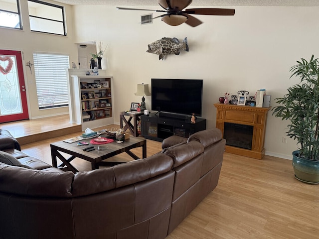 living room with ceiling fan, vaulted ceiling, a textured ceiling, and light wood-type flooring