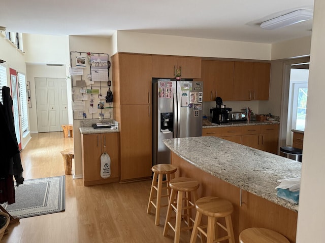 kitchen with light stone counters, stainless steel fridge with ice dispenser, a breakfast bar, and light wood-type flooring