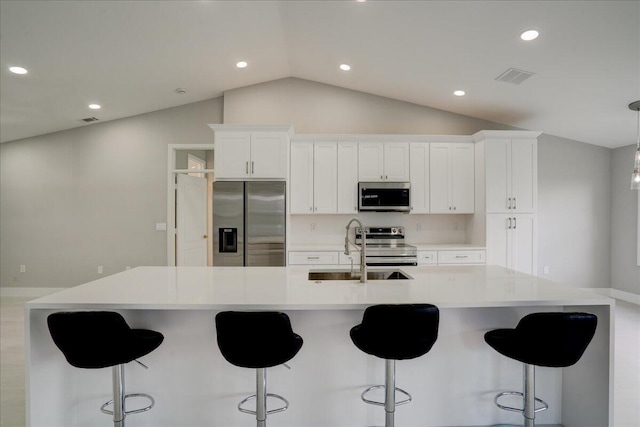 kitchen featuring vaulted ceiling, white cabinetry, sink, stainless steel appliances, and a large island with sink