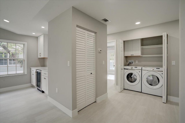 washroom with light hardwood / wood-style floors, cabinets, washer and clothes dryer, and wine cooler