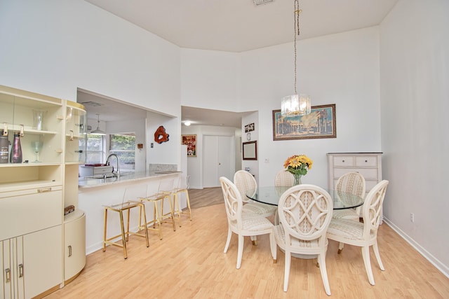 dining area featuring sink, a notable chandelier, a high ceiling, and light hardwood / wood-style floors