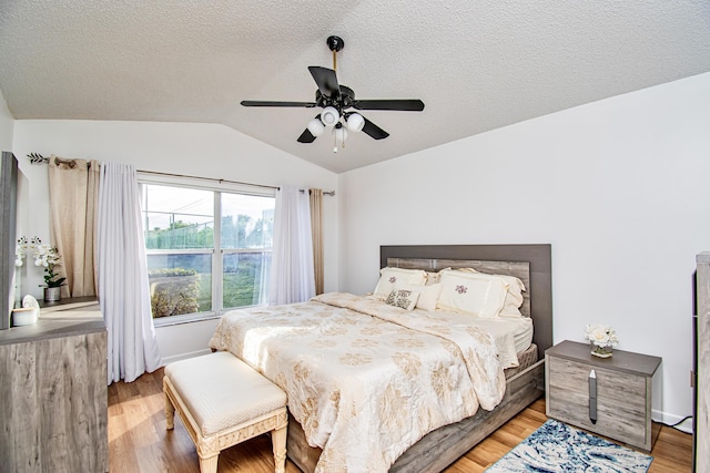 bedroom with ceiling fan, light hardwood / wood-style floors, a textured ceiling, and vaulted ceiling