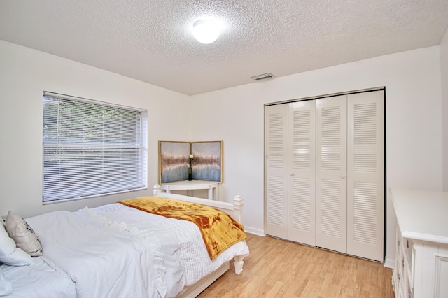 bedroom with light hardwood / wood-style floors, a textured ceiling, and a closet