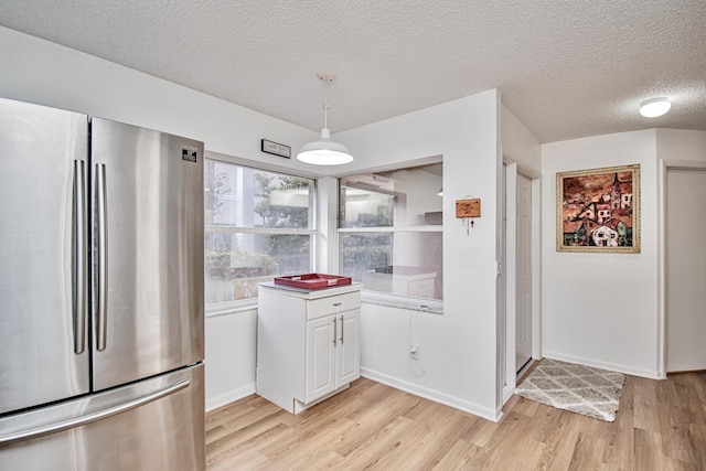 kitchen featuring a textured ceiling, white cabinets, decorative light fixtures, stainless steel refrigerator, and light hardwood / wood-style flooring