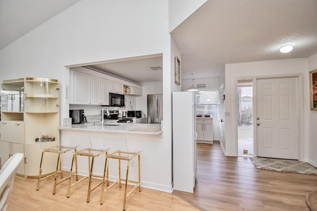 kitchen featuring appliances with stainless steel finishes, a textured ceiling, white cabinetry, kitchen peninsula, and a breakfast bar