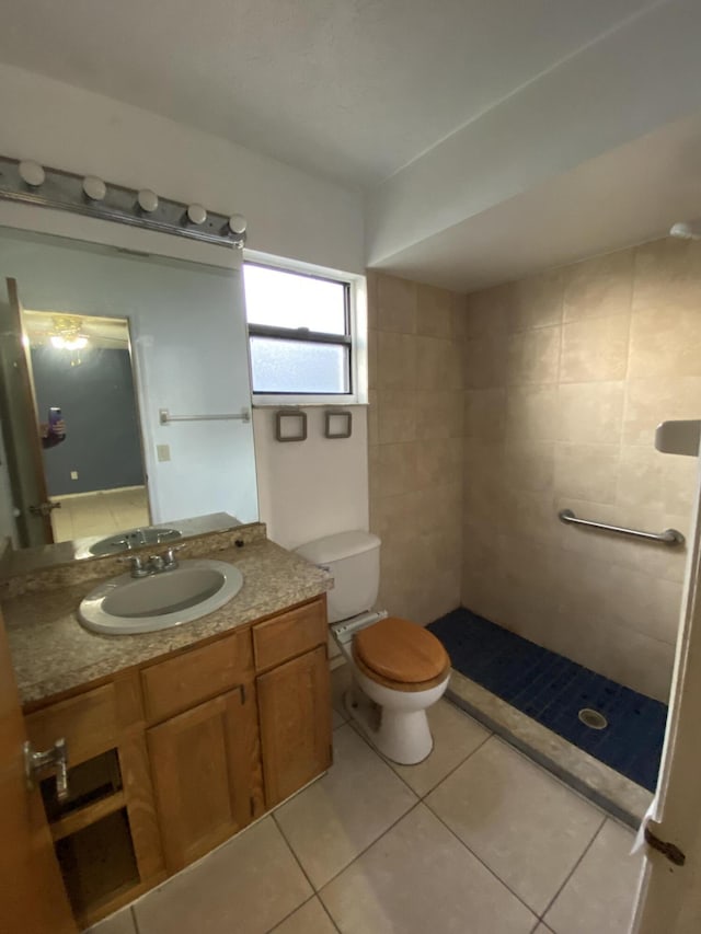 bathroom featuring toilet, tile patterned flooring, a tile shower, and vanity