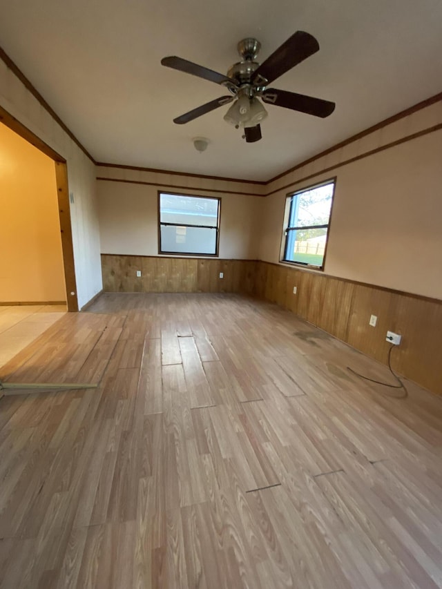 empty room with wooden walls, ceiling fan, light hardwood / wood-style floors, and crown molding