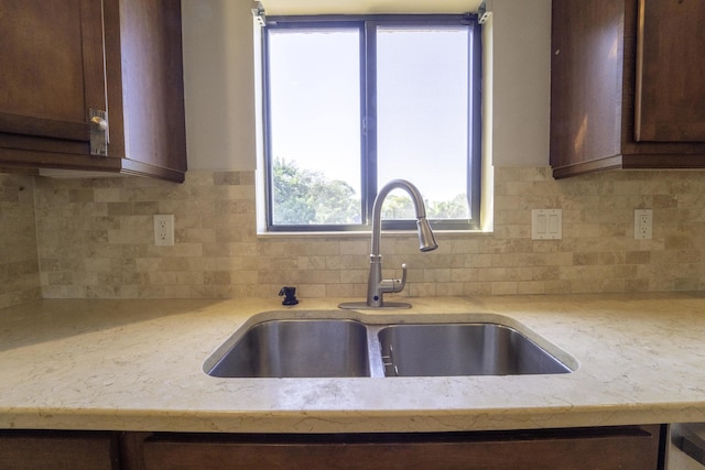 kitchen featuring sink, decorative backsplash, light stone countertops, and dark brown cabinetry