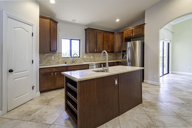 kitchen with sink, stainless steel appliances, light stone counters, lofted ceiling, and an island with sink