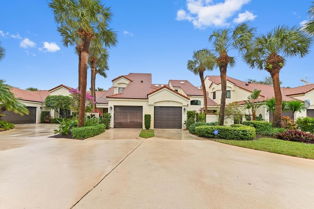 mediterranean / spanish-style home with an attached garage, a tile roof, concrete driveway, and stucco siding